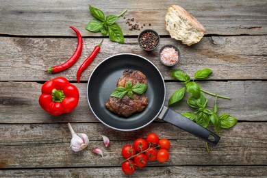Photo of Frying pan with tasty cooked steak and fresh vegetables on wooden table, flat lay