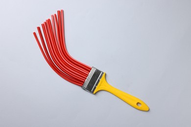 Brush with red straws on light grey background, top view. Creative concept