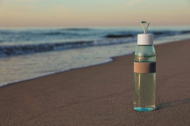 Photo of Glass bottle with water on wet sand near sea at sunset. Space for text