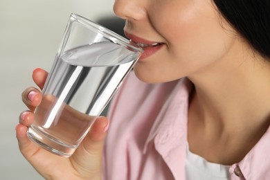 Photo of Young woman drinking water indoors, closeup. Refreshing drink
