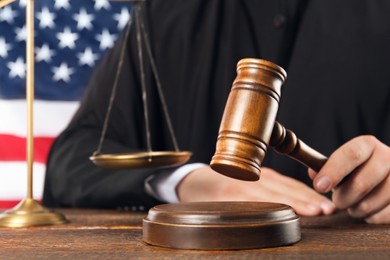 Judge with gavel at wooden table near flag of United States, closeup