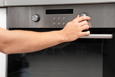 Photo of Young man adjusting oven settings in kitchen, closeup