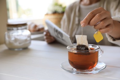 Photo of Woman taking tea bag out of cup at white wooden table indoors, closeup. Space for text