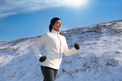 Happy woman running past snowy hill in winter. Outdoors sports exercises