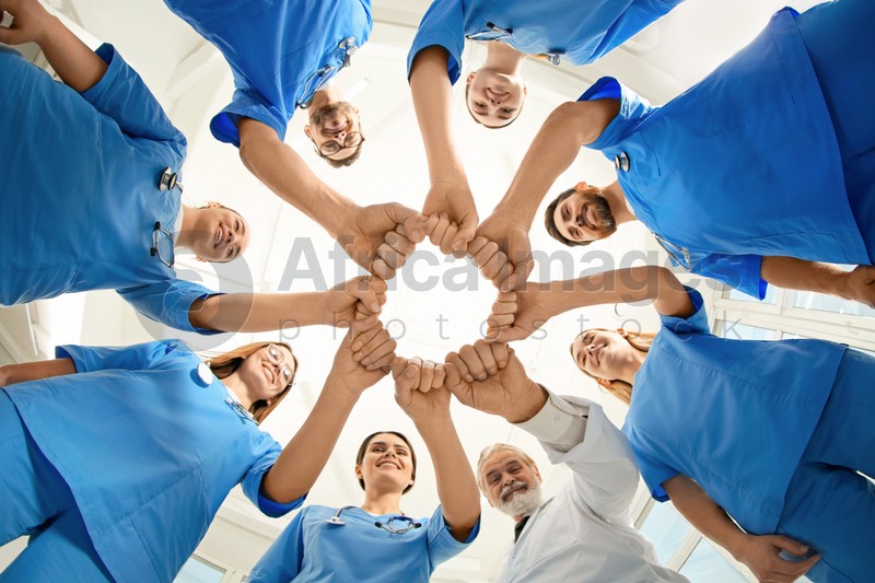 Photo of Doctor and interns holding fists together indoors, bottom view