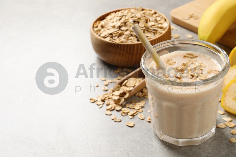 Glass of tasty banana smoothie with oatmeal on light grey table. Space for text