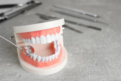 Model of jaw with teeth and dentist mirror on grey table, closeup. Space for text