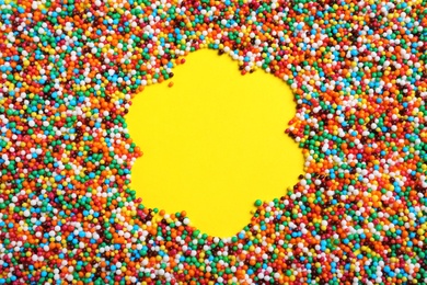 Flower shaped frame of bright colorful sprinkles on yellow background, flat lay with space for text. Confectionery decor