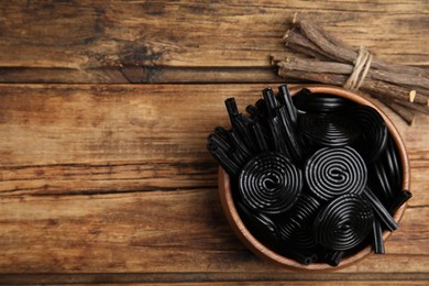 Tasty black candies and dried sticks of liquorice root on wooden table, flat lay. Space for text