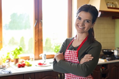 Photo of Portrait of happy young woman wearing apron in kitchen, space for text