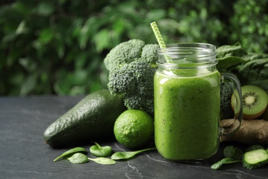 Photo of Delicious green juice and fresh ingredients on black table. Space for text
