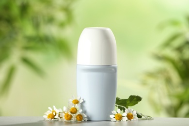Deodorant container and chamomile on white wooden table against blurred background