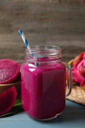 Delicious pitahaya smoothie in mason jar and fresh fruits on light blue wooden table, closeup