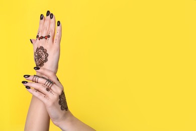 Woman with henna tattoos on hands against yellow background, closeup and space for text. Traditional mehndi ornament