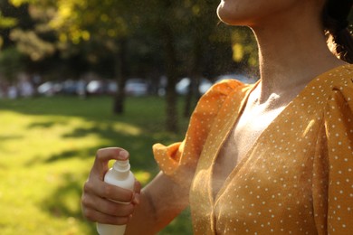 Photo of Woman applying insect repellent onto neck in park, closeup