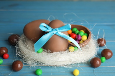 Composition with tasty chocolate eggs, colorful candies and decorative nest on light blue wooden table