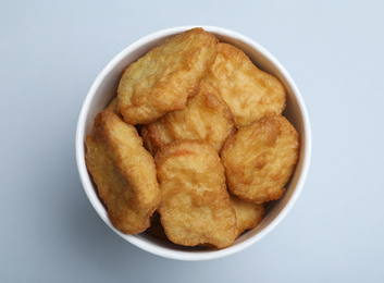 Bucket with delicious chicken nuggets on light background, top view