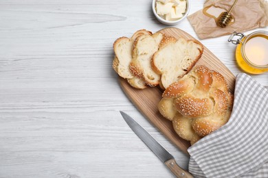 Cut freshly baked braided bread, honey and butter on white wooden table, flat lay with space for text. Traditional Shabbat challah