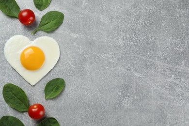 Photo of Heart shaped fried egg, tomatoes and spinach on light grey table, flat lay. Space for text