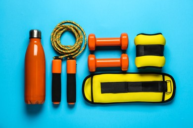 Yellow weighting agents and sport equipment on light blue background, flat lay