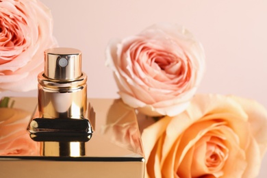 Bottle of perfume and fresh roses on beige background, closeup
