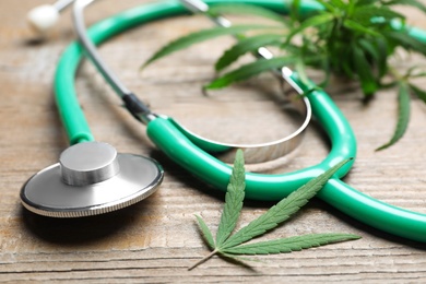 Hemp leaves and stethoscope on wooden table, closeup