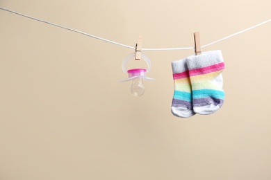 Small socks and pacifier hanging on washing line against color background, space for text. Baby accessories