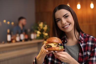 Photo of Young woman eating tasty burger in cafe