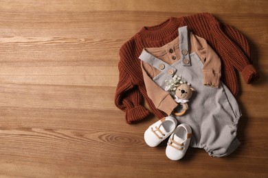 Children's shoes, clothes and toy on wooden table, flat lay. Space for text