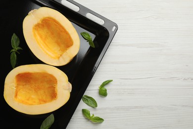 Sheet pan with raw spaghetti squash halves and basil on white wooden table, flat lay. Space for text
