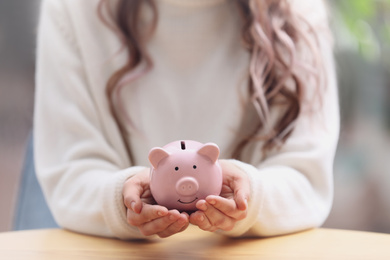 Woman holding piggy bank at table, closeup