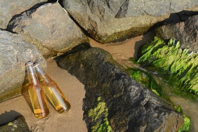 Bottles of cold beer near rocks on sandy beach, space for text
