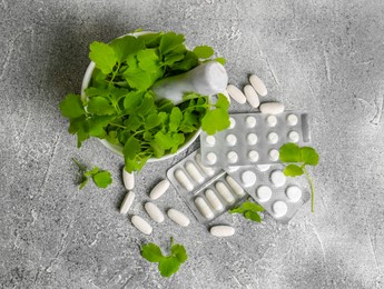Mortar with fresh green celandine and pills on light grey table, flat lay