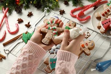 Making homemade Christmas cookies. Girl decorating gingerbread man at white wooden table, closeup