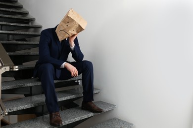 Man wearing paper bag with drawn sad face indoors. Space for text