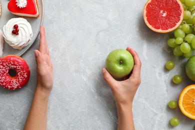 Photo of Concept of choice. Top view of woman holding apple at grey table, closeup