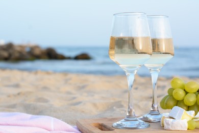 Glasses with white wine and snacks on sandy seashore. Space for text