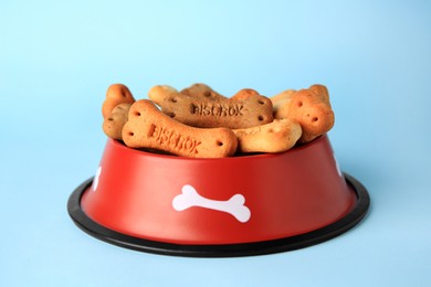Photo of Bone shaped dog cookies in feeding bowl on light blue background