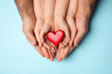 Parents and kid holding red heart in hands on light blue background, top view