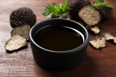 Photo of Fresh truffle oil in bowl on wooden table, closeup