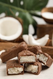 Delicious milk chocolate candy bars with coconut filling on white wooden table, closeup. Space for text