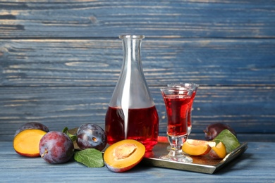 Delicious plum liquor and ripe fruits on blue wooden table. Homemade strong alcoholic beverage