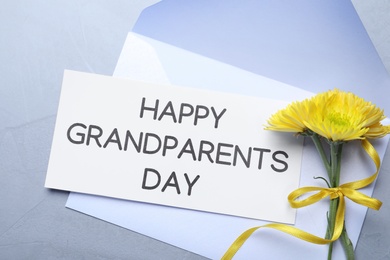 Card with phrase Happy Grandparents Day, envelope and beautiful flowers on grey background, flat lay