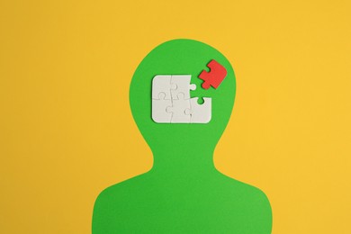 Photo of Human paper cutout with jigsaw puzzles in head, red piece as solution idea on yellow background, flat lay