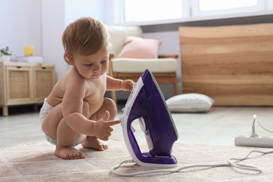 Photo of Cute baby playing with iron on floor at home. Dangerous situation