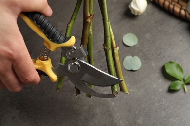 Florist cutting flower stems with pruner at grey stone table, closeup
