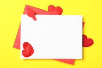 Blank card, envelope and red decorative hearts on yellow background, flat lay with space for text. Valentine's Day celebration