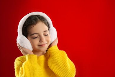 Cute girl wearing stylish earmuffs on red background. Space for text