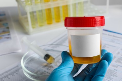 Photo of Nurse holding container with urine sample at table, closeup and space for text. Specimen collection