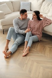 Happy couple sitting on warm floor in living room. Heating system